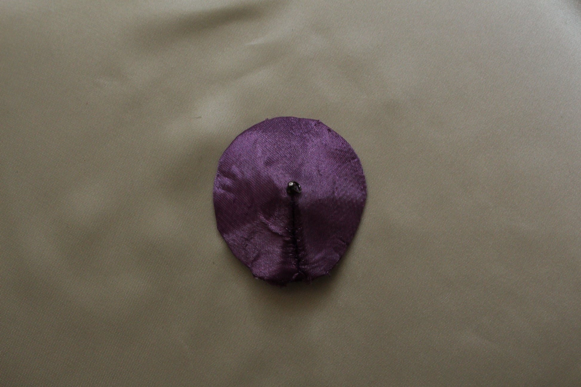 A single Round Purple satin pasties on a cream background 